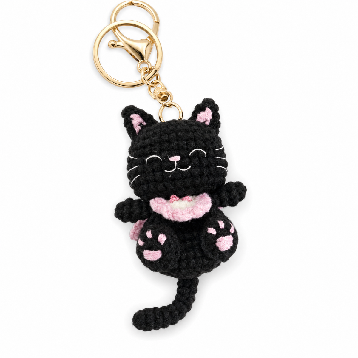 Close up of a black crochet cat keychain with embroidered squinting eyes and gold-tone lobster clasp.