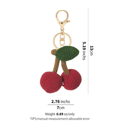 A hand-crochet cherry keychain with two red spheres, brown stems, and a green leaf, shown with dimension labels.